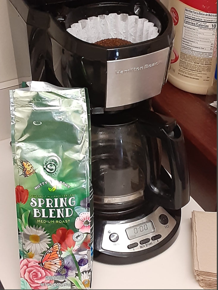 Open bag of coffee sits in front of a coffee pot.